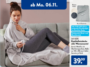 Frau auf einem grauen Sofa sitzend, die sich gemütlich in eine EASY HOME Kuschelheizdecke eingewickelt hat und die Heizfunktion über ein Handgerät steuert."